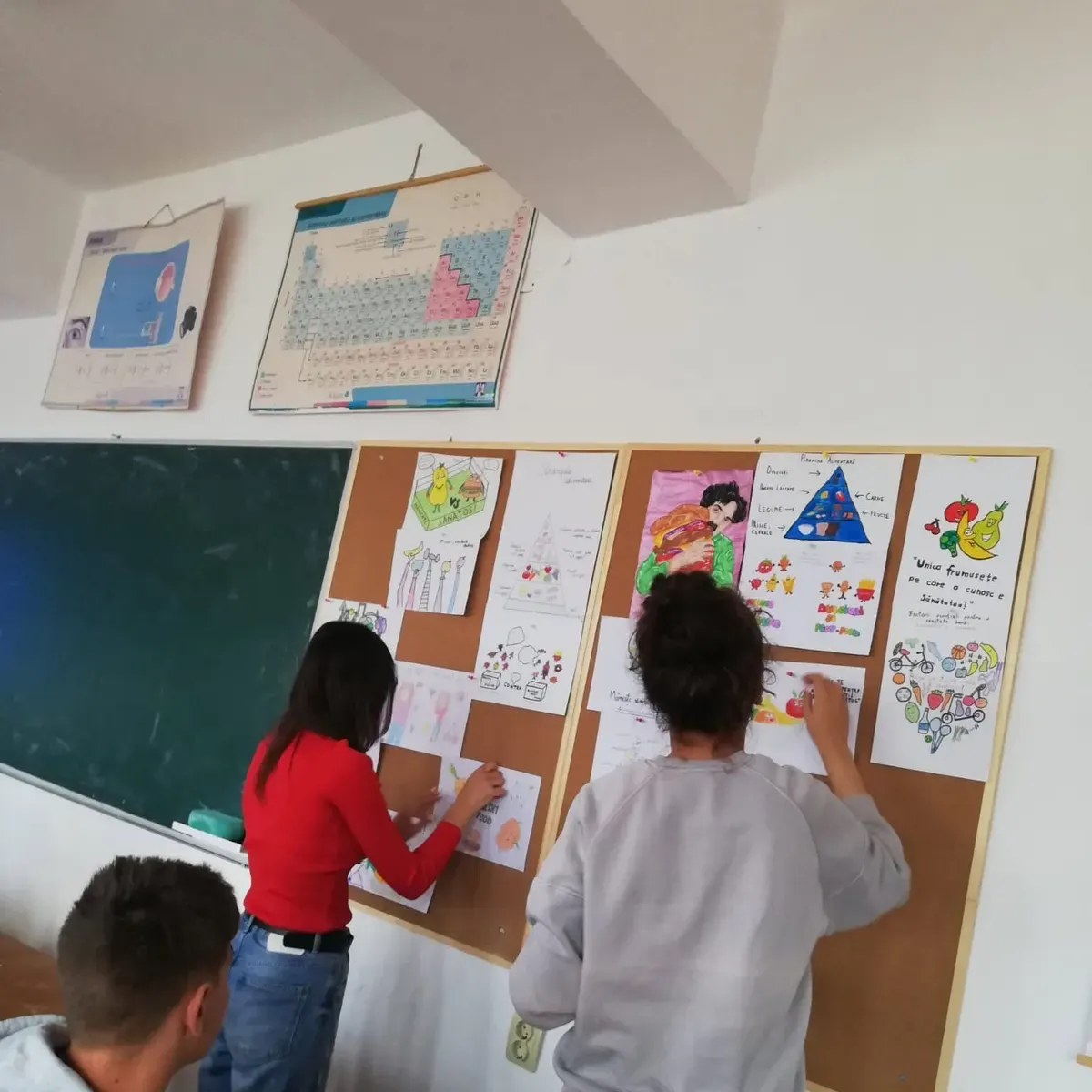 Students arranging their classmates' work on classroom pinboards
