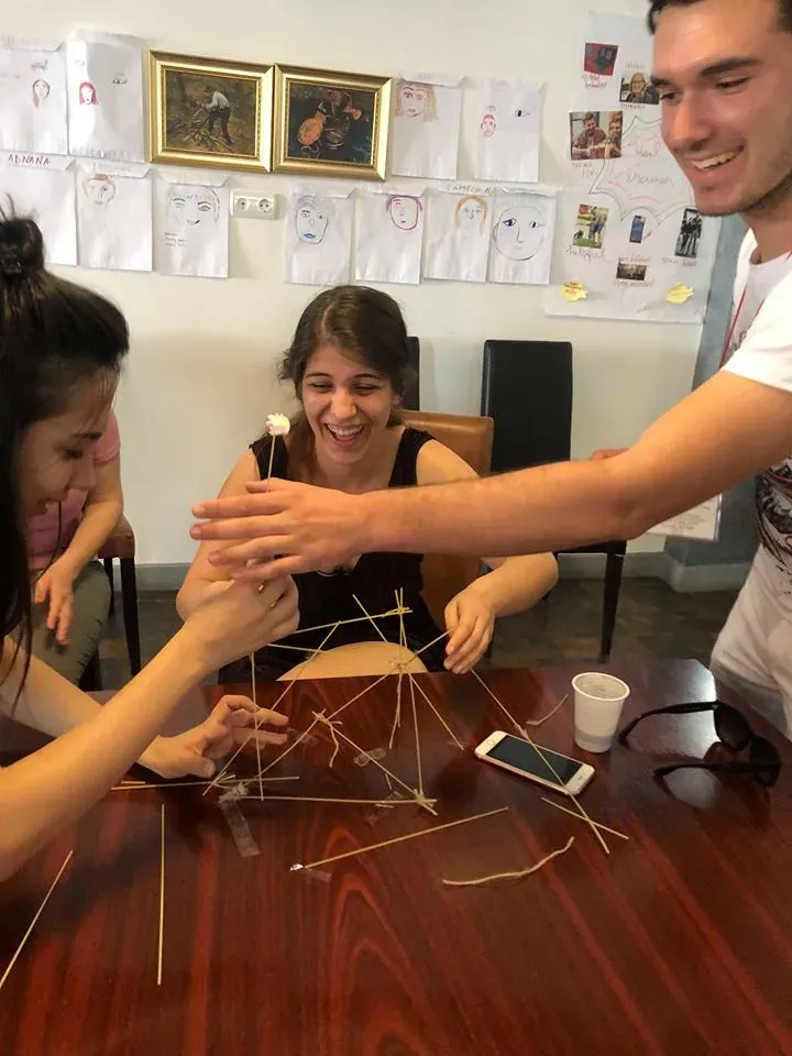 Three participants laughing as they build a spaghetti-and-marshmallow tower in a team-building game