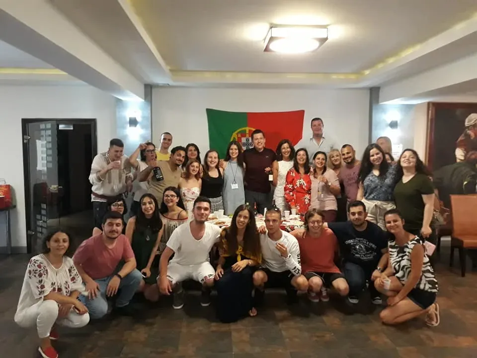 The international group of participants gathered for a group photo in front of a Portuguese flag